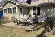 Thumbnail for Backyard patio with outdoor table, chairs, grill, and beige siding house under a clear sky.