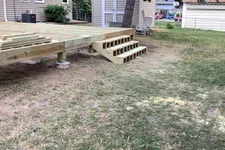 Thumbnail for Partially constructed wooden deck with steps in a backyard near houses and a large tree