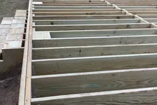 Thumbnail for Wooden deck frame construction next to house with visible joists and stairs framed in backyard.