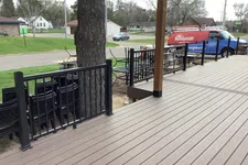Thumbnail for Spacious wooden deck with black metal railing, tree, and a red Mr. Handyman van parked on the street nearby.