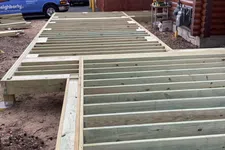 Thumbnail for Wooden deck frame construction beside a log cabin on a residential property with work vans nearby