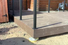 Thumbnail for Newly constructed brown wooden deck with black metal posts attached to a log cabin exterior door.