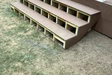 Thumbnail for Three-step brown wooden outdoor stairs attached to a deck with visible support structure on dry lawn.