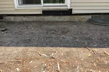 Thumbnail for Cleared backyard ground with dirt and wood debris outside a house with beige siding and sliding glass door.
