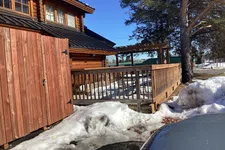 Thumbnail for Snow-covered ground around a wooden cabin with a porch railing and clear blue sky on a sunny day.