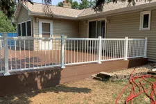 Thumbnail for Raised brown wooden deck with white railings attached to beige house under tree shade in backyard.