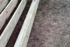 Thumbnail for Wooden deck frame under construction on a soil and grass surface with concrete footings.
