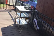 Thumbnail for Outdoor deck with metal work table, tools, a Coca-Cola cup, and a handyman service van parked nearby on a sunny day.