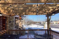 Thumbnail for Snow-covered outdoor patio with wooden pergola, string lights, and black metal tables and chairs in a commercial area.