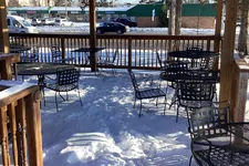 Thumbnail for Snow-covered outdoor patio with metal tables and chairs under a wooden pergola on a sunny winter day.