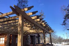 Thumbnail for Wooden pergola with string lights on a porch of a log cabin house under clear blue sky in winter.