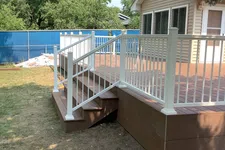 Thumbnail for Backyard wooden deck with white railing and steps attached to beige house under trees.