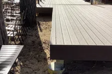 Thumbnail for Newly constructed wooden deck beside a log cabin with chairs and a large tree nearby on a sunny day.