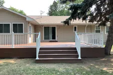 Thumbnail for Backyard wooden deck with white railing and stairs attached to beige house with sliding glass door.