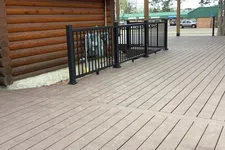 Thumbnail for Brown wooden deck next to log cabin with black metal railing and broom on the ground in daytime.