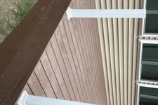 Thumbnail for Newly built brown wooden deck attached to beige house with white support posts and large windows.