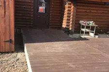 Thumbnail for Newly built raised wooden deck attached to a rustic log cabin with a metal roof and a dark door.