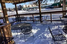 Thumbnail for Snow-covered outdoor patio seating with metal tables and chairs under wooden pergola on a sunny winter day.