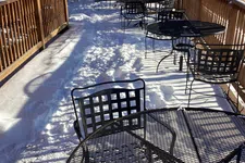 Thumbnail for Outdoor patio with black metal tables and chairs covered in snow on a sunny winter day.