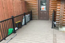 Thumbnail for Spacious wooden deck with black metal railing leading to a brown door on a log cabin exterior.