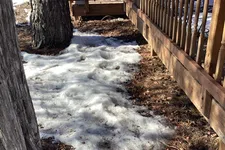 Thumbnail for Melting snow on the ground next to a wooden deck and trees on a sunny day in late winter.