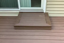 Thumbnail for Brown wooden deck with a single step leading up to sliding glass door and light beige siding on house.