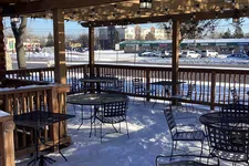 Thumbnail for Outdoor patio with metal tables and chairs covered in snow under a wooden pergola on a bright winter day.