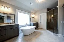 Thumbnail for Modern bathroom with freestanding tub, dual vanities, large window, and glass-enclosed shower with tiled floor.
