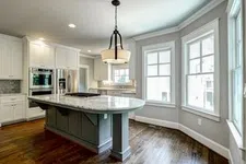Thumbnail for Bright modern kitchen with large marble island, white cabinets, stainless steel appliances, hardwood floors, and large windows