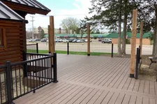 Thumbnail for Spacious wooden deck with black metal railings and vertical posts next to a log cabin under a blue sky.
