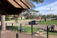 Thumbnail for Outdoor deck under construction near a road with a man working and a parked SUV on a sunny day.