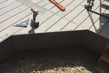 Thumbnail for Wooden deck under construction with power drill, level, and rocky ground below the deck frame.