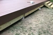 Thumbnail for Newly built brown wooden backyard deck with stairs next to house and garden shed on grassy ground.