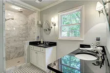 Thumbnail for Modern bathroom with marble shower, dual sinks with black countertops, white cabinetry, and natural light from window.