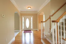 Thumbnail for Bright entryway with wooden floors, staircase with carpeted steps, beige walls, and white door with oval glass window.