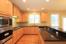 Thumbnail for Modern kitchen with wooden cabinets, black granite countertops, stainless steel appliances, and hardwood flooring.