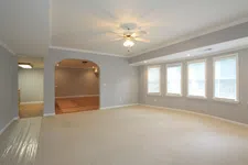 Thumbnail for Bright empty living room with beige carpet, gray walls, ceiling fan, and three large windows with blinds.