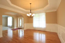Thumbnail for Empty dining room with hardwood floors, beige walls, white wainscoting, chandelier, and a window with sheer curtains