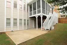 Thumbnail for House exterior with beige siding, concrete patio, white screened porch, and stairs leading to backyard.