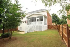 Thumbnail for Backyard view of a house with a white screened porch and wooden fence surrounding the grassy yard.