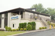 Thumbnail for Modern two-story Lakeview building with stairs, railings, greenery, and a parking lot under an overcast sky