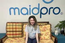 Thumbnail for Smiling woman in MaidPro shirt sitting on floral patterned couch under MaidPro logo on white wall