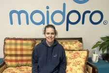 Thumbnail for Woman in a MaidPro uniform sitting on a vintage floral sofa under a MaidPro logo on a white wall.