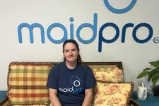 Thumbnail for Woman in Maid Pro uniform sitting on floral patterned couch with Maid Pro logo on wall behind her.