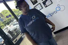Thumbnail for Woman standing inside MaidPro office wearing a MaidPro t-shirt near certificates and window.