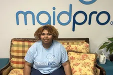 Thumbnail for Woman with curly hair sitting on a floral patterned sofa in front of a MaidPro logo wall sign.