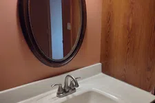 Thumbnail for Bathroom sink with silver faucet, oval framed mirror, peach wall, and wood paneling under soft light.