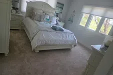 Thumbnail for Bright white bedroom with a large bed, bedside tables, soft carpet, and three windows letting in natural light.