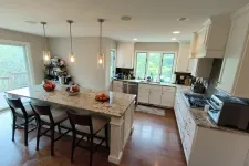 Thumbnail for Modern kitchen with white cabinets, granite island countertop, wooden floor, and large windows overlooking greenery.