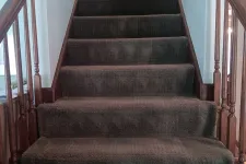 Thumbnail for Brown carpeted staircase with wooden handrails and white walls on both sides in a residential interior.